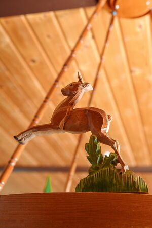 Geschnitzte Holzfigur eines springenden Rehs vor einer Holzdecke