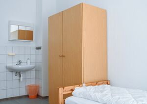 Einzelzimmer mit Waschbecken, Spiegelschrank und Kleiderschrank