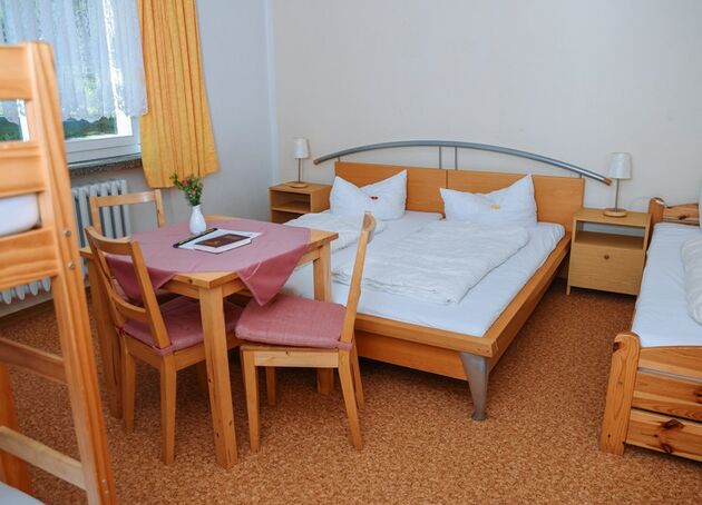 Zimmer mit Doppelbett, Einzelbett und Tisch mit zwei Stühlen