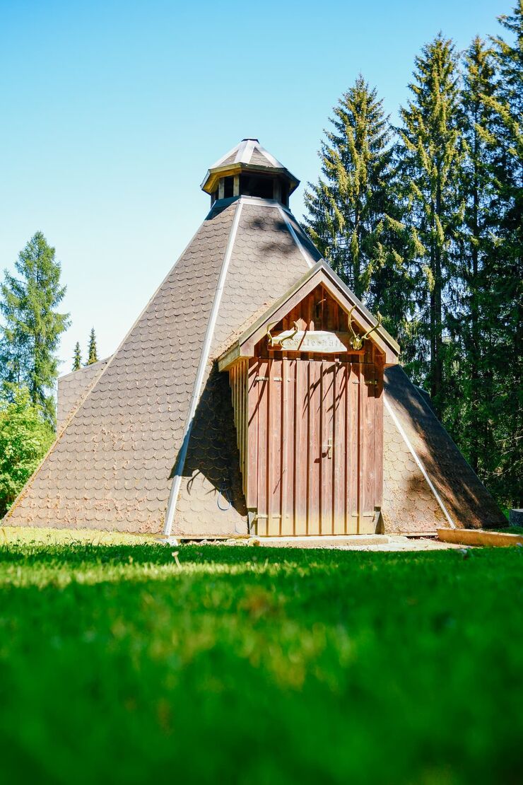 Die Köhlerhütte: pyramidenförmige Hütte mit Schindeldach und Holztür zwischen Fichten
