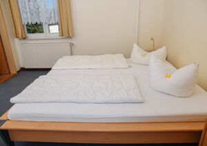 Doppelzimmer mit hellem Doppelbett vor dem Fenster