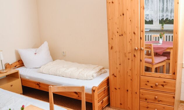 Einzelzimmer mit Holzbett, Nachttisch und Kleiderschrank aus Kiefernholz